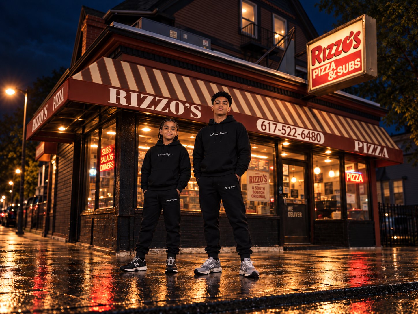 Two people wearing black Charly Bryan hoodies and joggers outside Rizzo’s in a Jamaica Plain campaign scene.